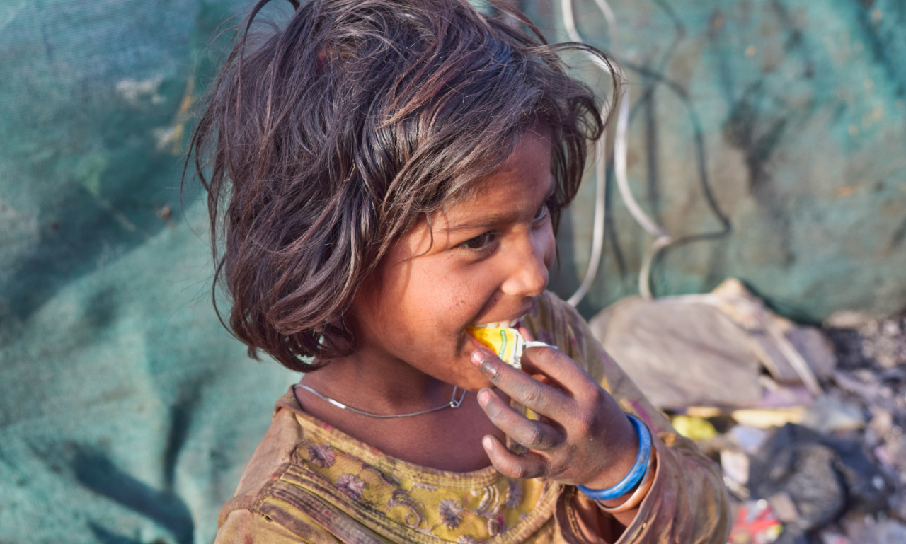 A young girl in a slum eating a small snack — a child every meal parcel is meant to reach